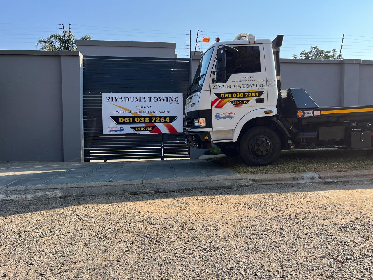 Ziyaduma Towing truck at the company premises, next to a gate sign reading 'Stuck? We'll get you rolling again'
